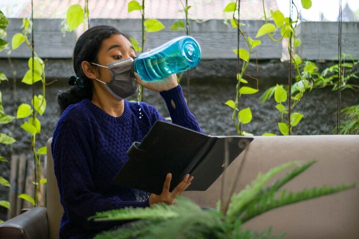 Young woman reading a book and try to drink when she still wearing a mask