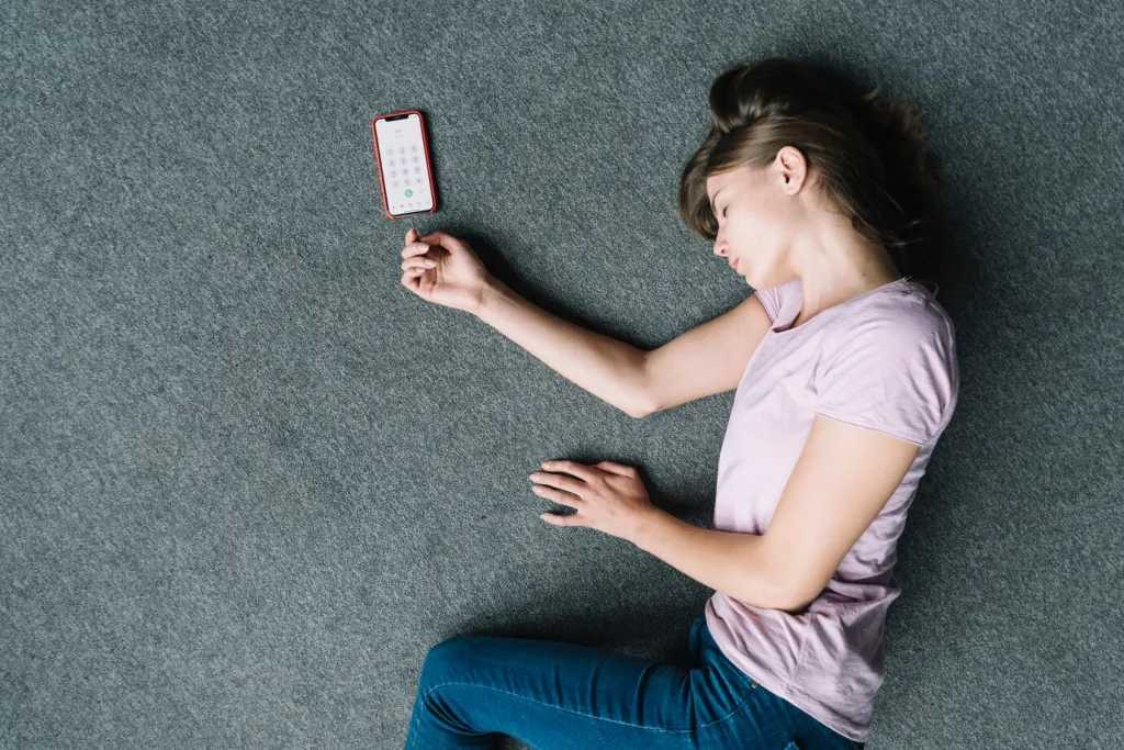 Overhead view of unconscious woman lying near cell phone on carpet