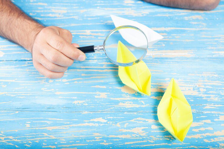 The guy looks at the paper boats with a magnifying glass