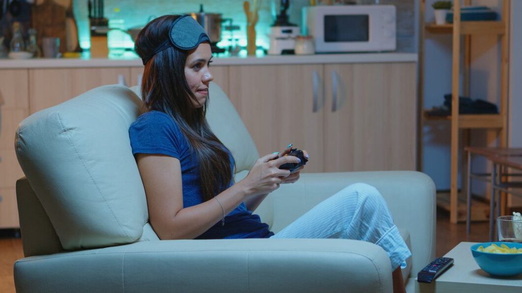 Gamer woman playing video games on console using controller and joysticks sitting on couch