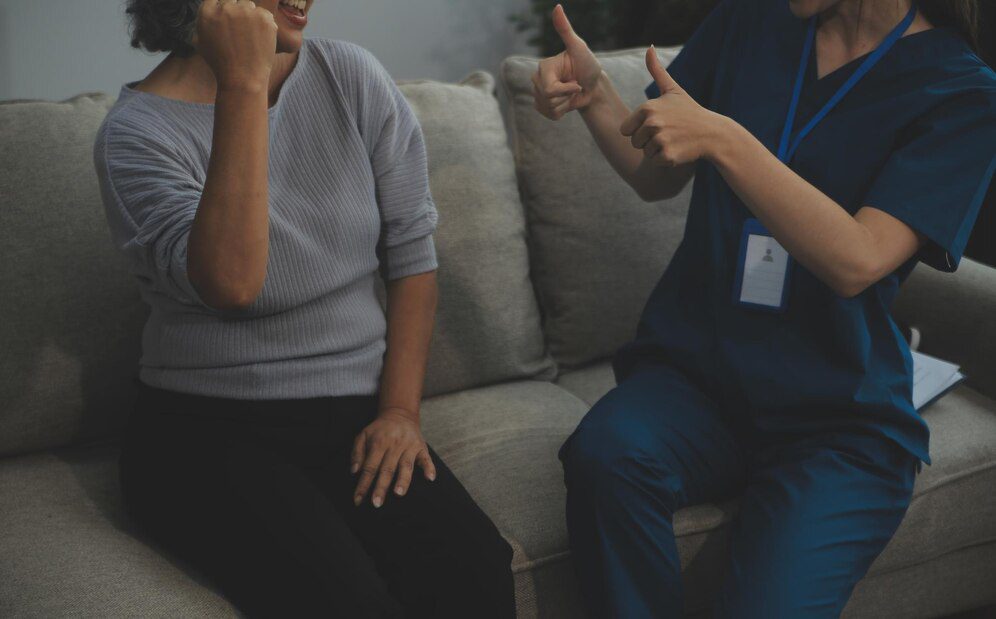 Smiling kind pleasant young female doctor in white uniform visiting disabled elderly mature patient