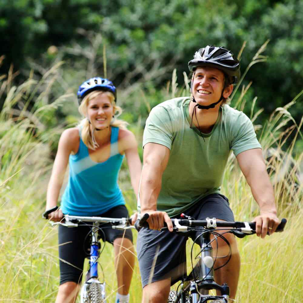 Two cyclists riding bikes on a grassy trail, following tips for a healthy lifestyle in NYC.