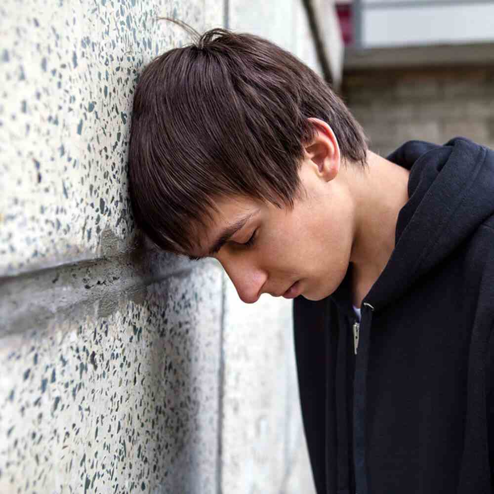 Person in a hoodie leaning against a wall, reflecting on suicide prevention activities in NYC.