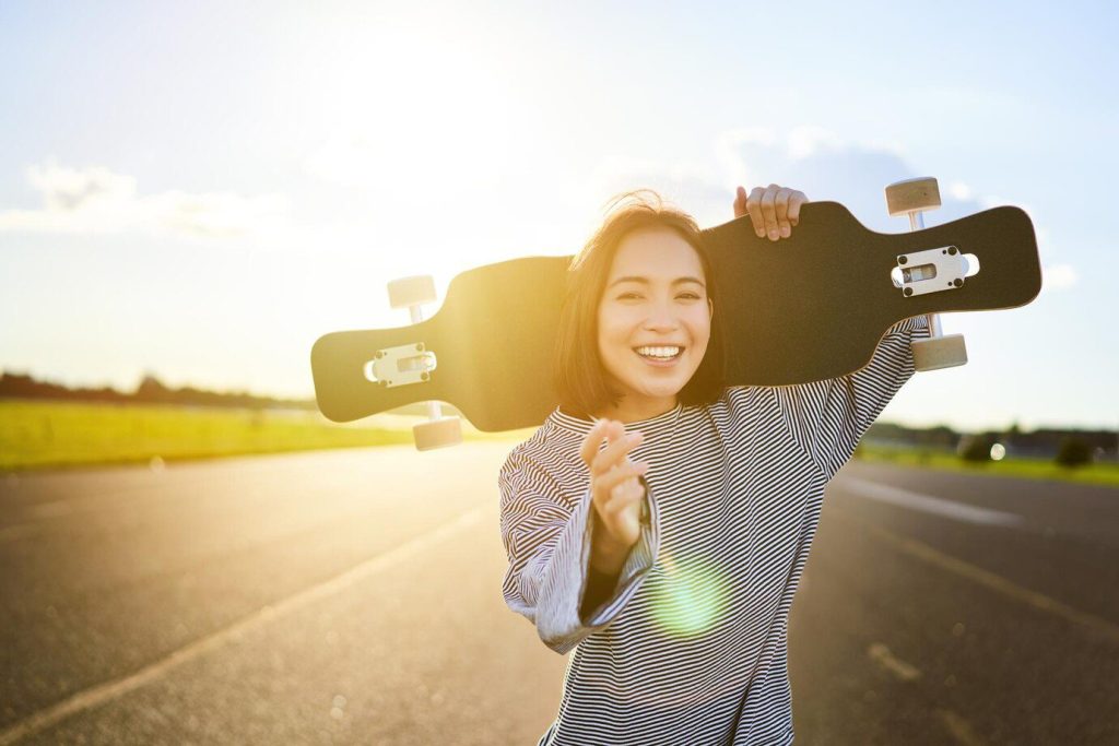 Happy skater girl walking towards the camera sunbeams shining at lense young woman skating on cruise