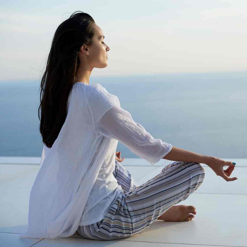 Woman meditating by the sea, embracing mindfulness in NYC.