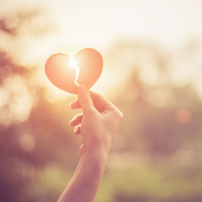 Hand holding a paper heart against a sunset, representing stages of breakup grief in NYC.