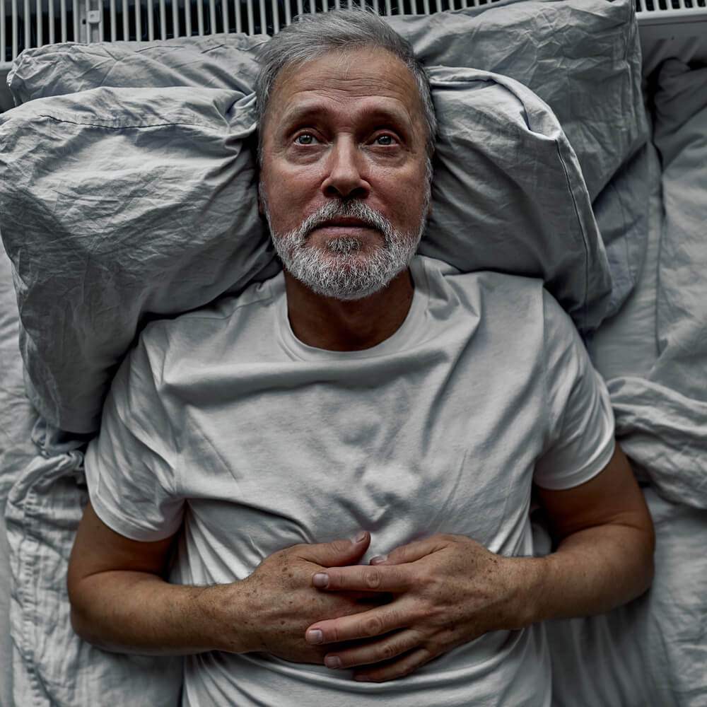 Person in a white shirt lying in bed, dealing with anxiety about death in NYC.