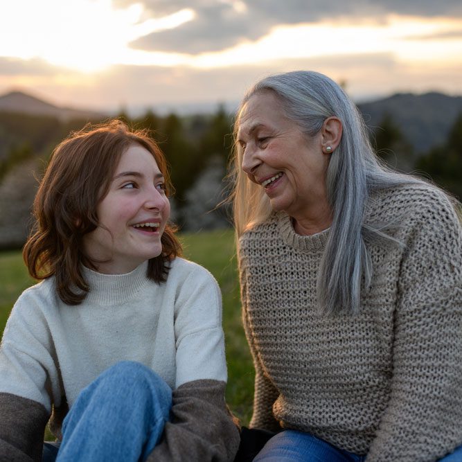 Happy senior grandmother with teenage granddaguhter sitting on grass