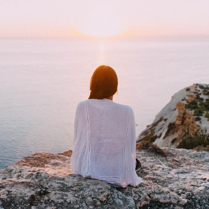 woman sitting on cliff watching sea