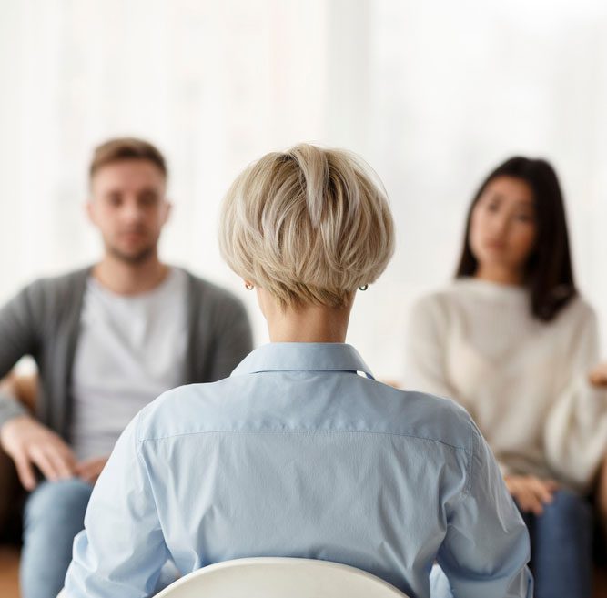 Professional Psychologist Sitting Back To Camera During Appointment With Unhappy Couple In Office.
