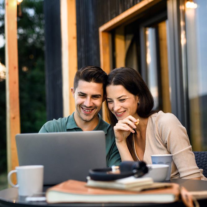 Young couple with laptop outdoors, weekend away in container house in countryside.