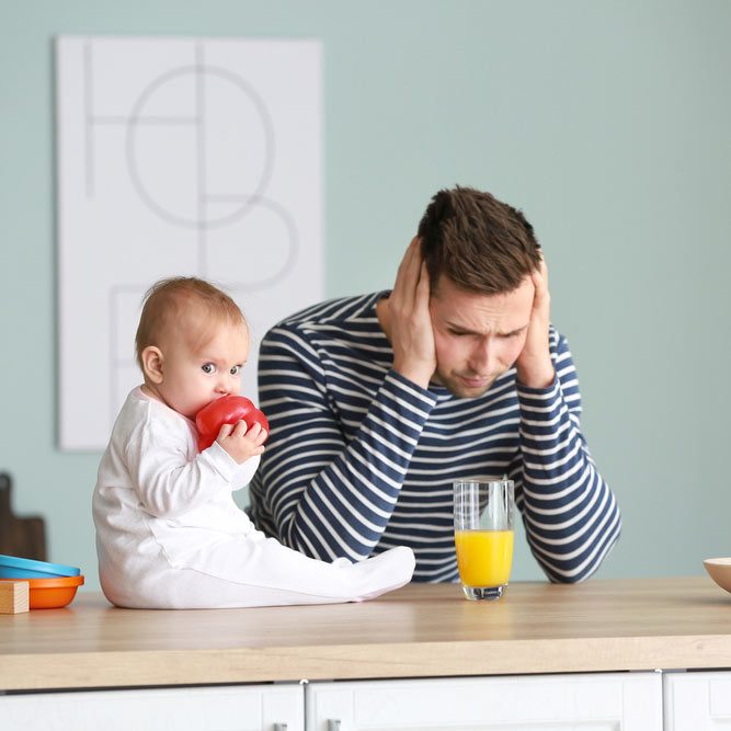 Young man suffering from postnatal depression in kitchen