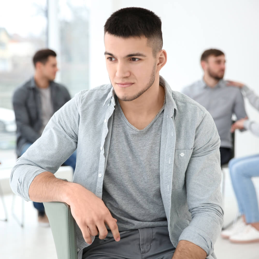 Man in a gray shirt sitting with others, exploring CBT for social anxiety in NYC.