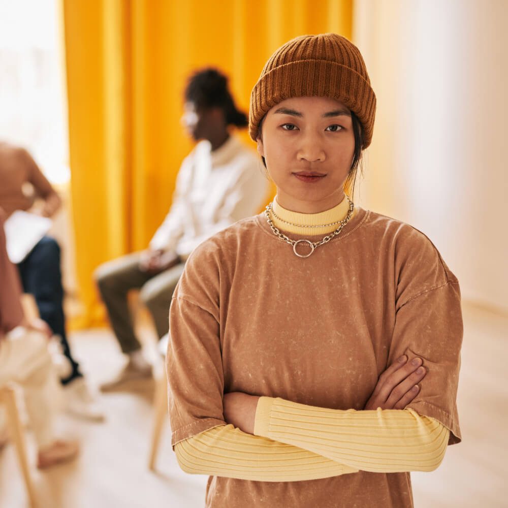 Person with crossed arms in brown attire, discussing mental health in Asian culture, NYC.