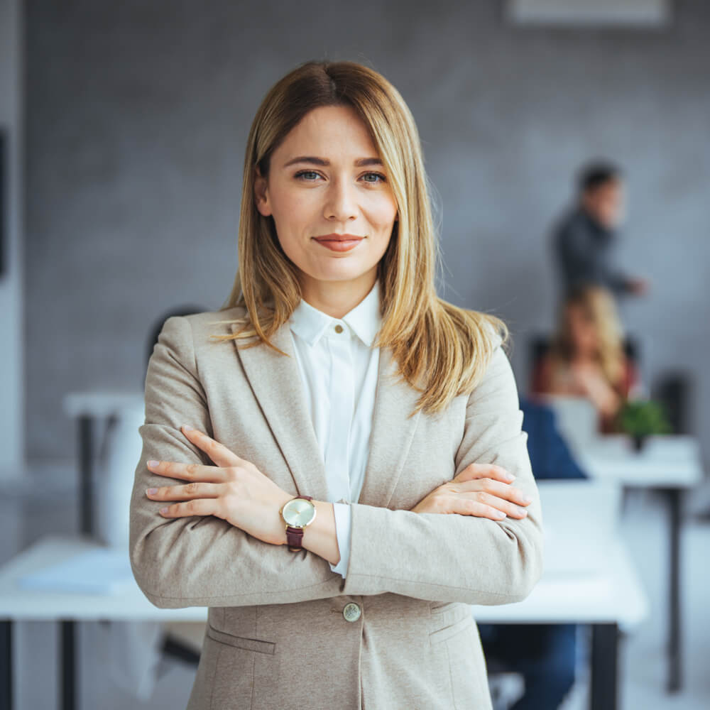 Woman in a beige suit with crossed arms, showing independence in an NYC office setting.