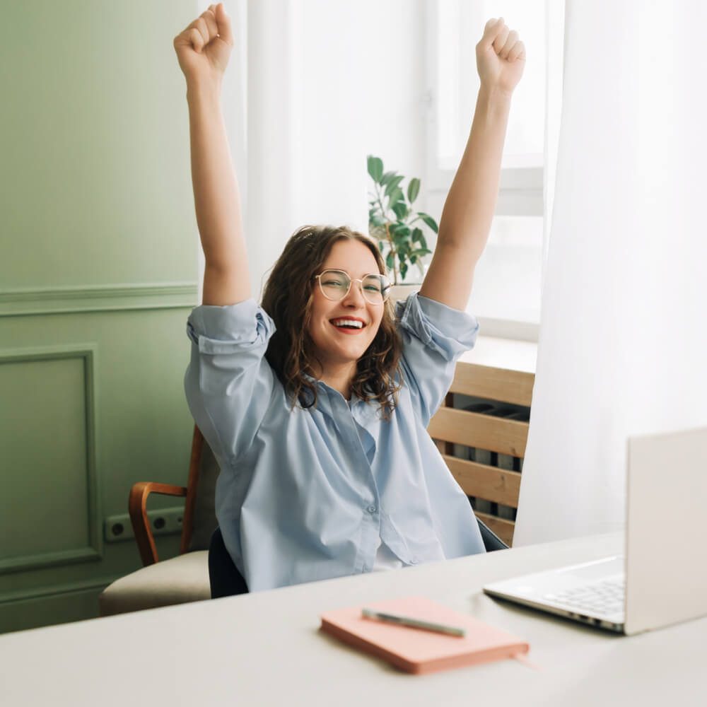 Person with raised arms at a desk with a laptop, focusing on improving employee well-being in NYC.