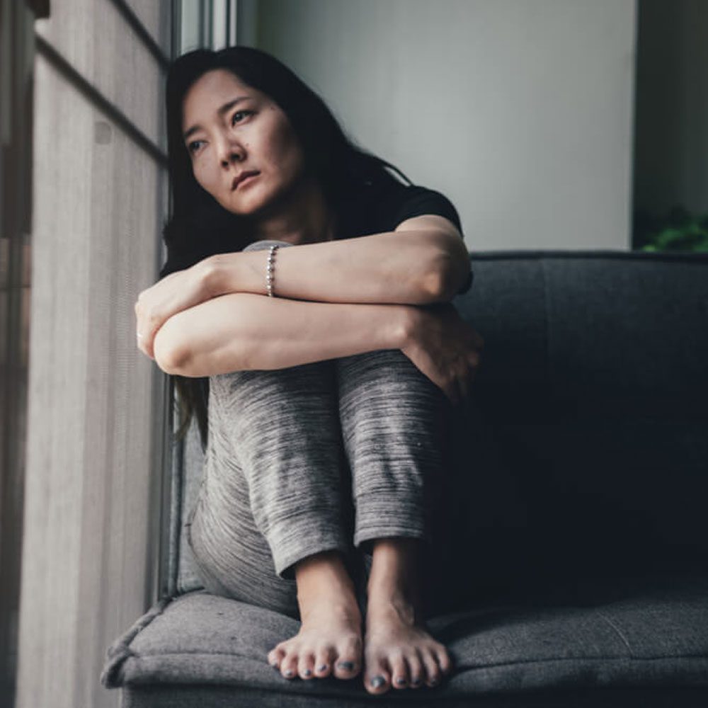 Person sitting on a couch hugging their knees, using affirmations for anxiety in NYC.