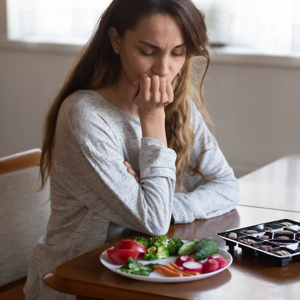 Person at a table with vegetables and chocolates, indicating eating disorder genetics in NYC.