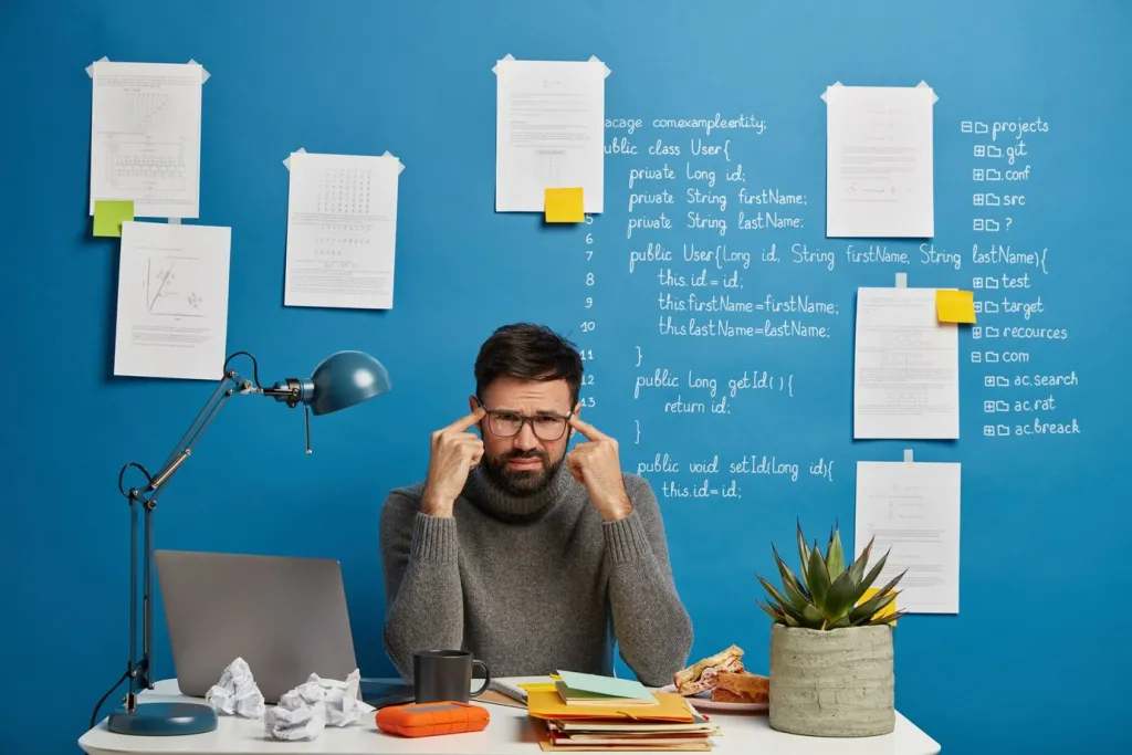 Unhappy male worker in spectacles sits at desktop during hard workday