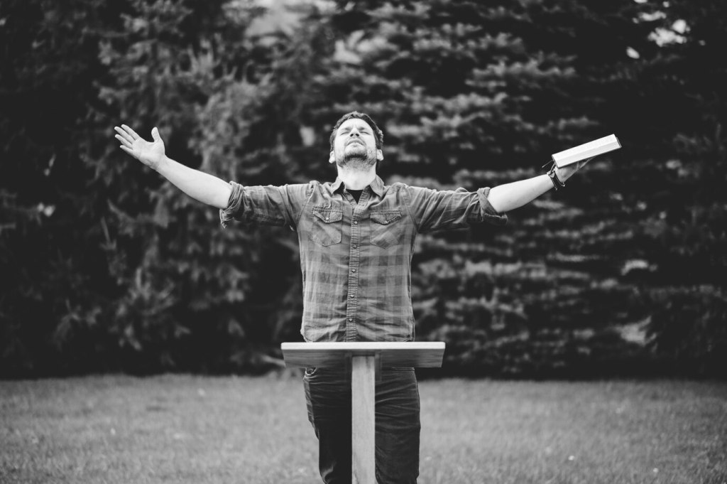 A grayscale shot of a Christian male holding the bible while praying