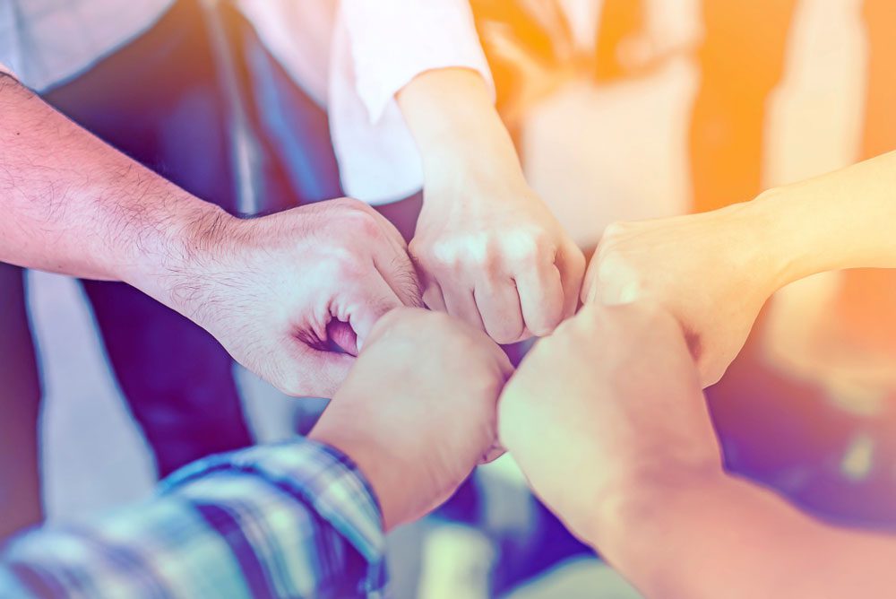 Team joining fists in a circle, symbolizing teamwork and striving for excellence in NYC