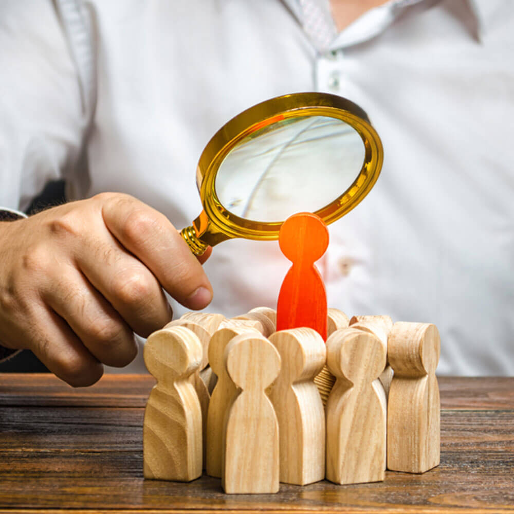 Magnifying glass on a red figure among wooden figures, highlighting signs of a toxic person in NYC.