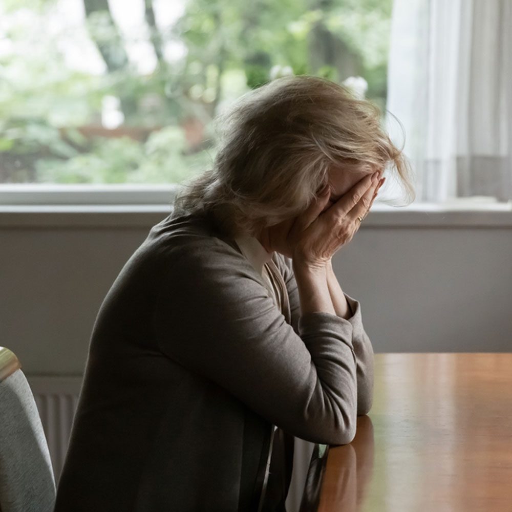 Distressed woman sitting with face in hands, exploring the need to cry in NYC - Uncover Counseling.