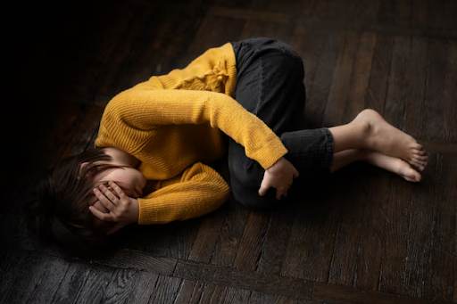Child curled up on wooden floor, face hidden, symbolizing struggle with depression.