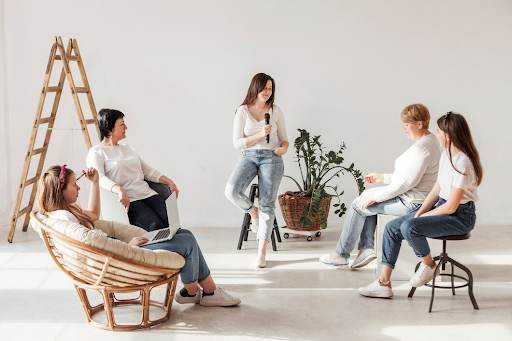 Individuals in a bright room with casual attire, with a plant and ladder in the background.