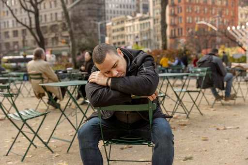 Person sitting with head down, surrounded by empty chairs and tables.