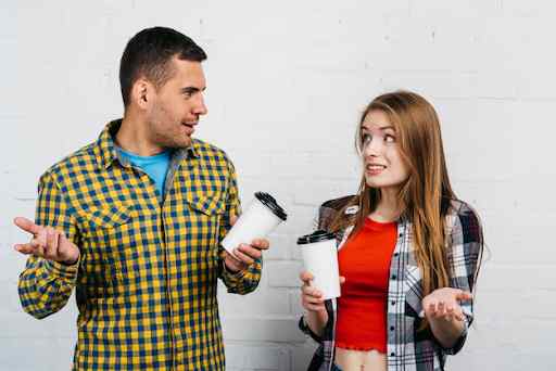 Two individuals holding coffee cups against a white brick wall background.