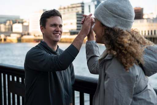 Two people giving a high five by a waterfront railing with the cityscape.