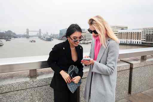 Two women standing by a railing with a river and bridge in the background.