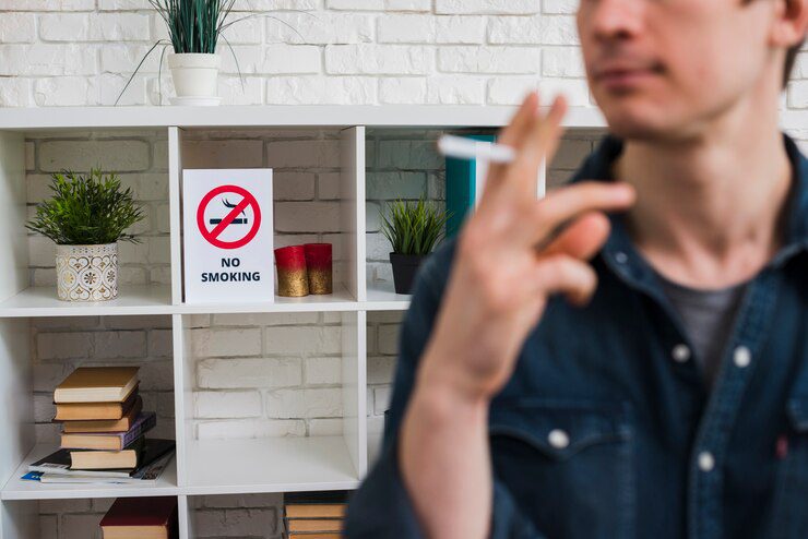 Image of a man with cigarette in front of no-smoking poster, highlighting smoking cessation efforts.
