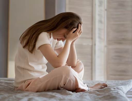 Distressed person sitting on bed with head in hands, showing a gesture of despair or sadness.