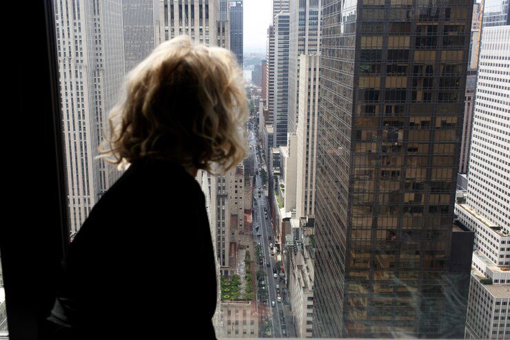 Seductive woman in black silk robe sits on a windowsill looking at New York