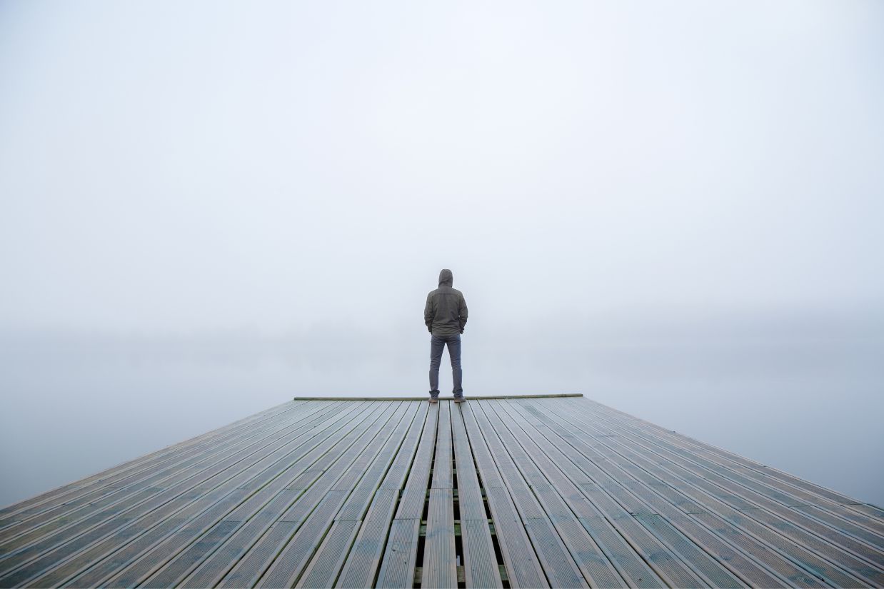 Person standing at the end of a foggy pier overlooking water.
