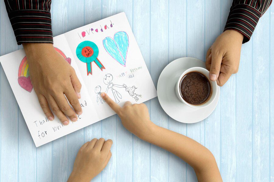 Little child saying thank you with greeting card while her father holding a cup of coffee, wooden background
