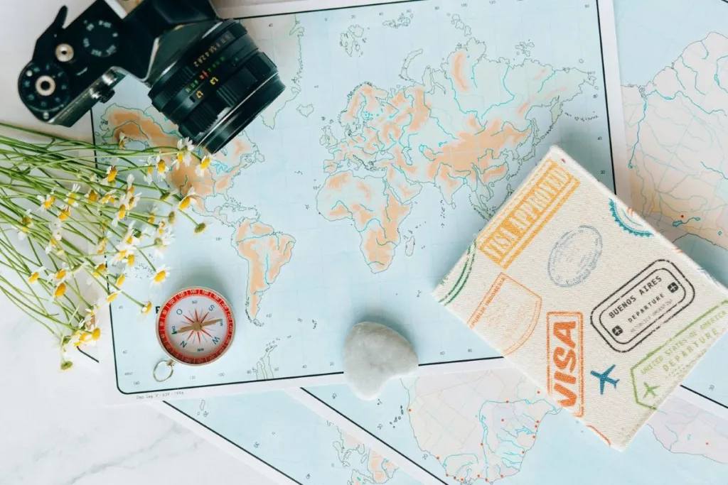 A vintage camera, compass, flowers, and a travel passport on world maps.