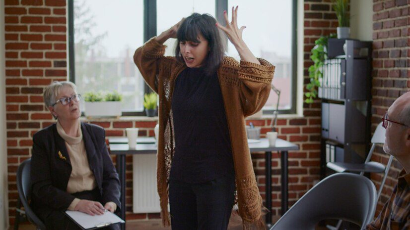 Woman having anger crisis in front of group of people and psychologist at aa therapy session.