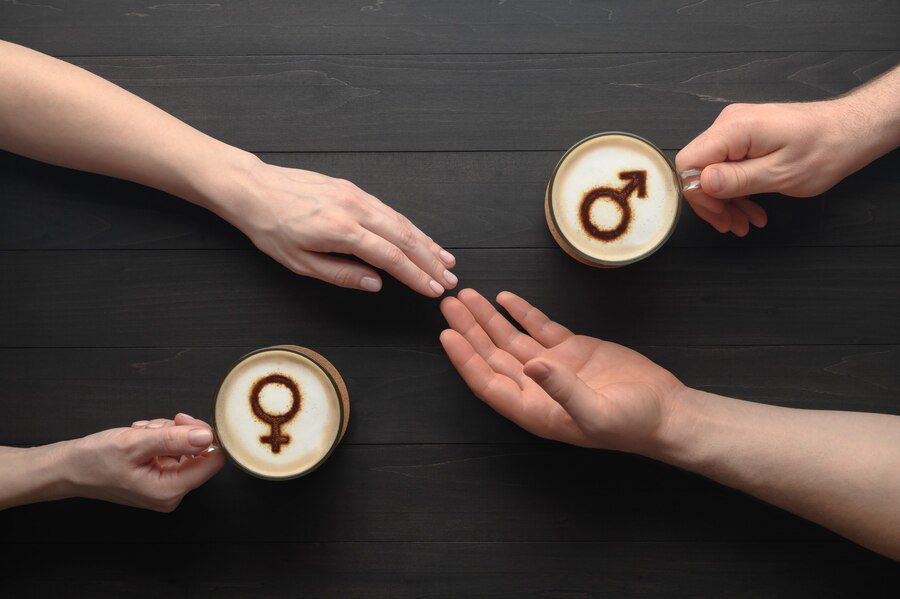 Two cups of coffee with symbols of venus and mars on milk foam and holding hands of couple