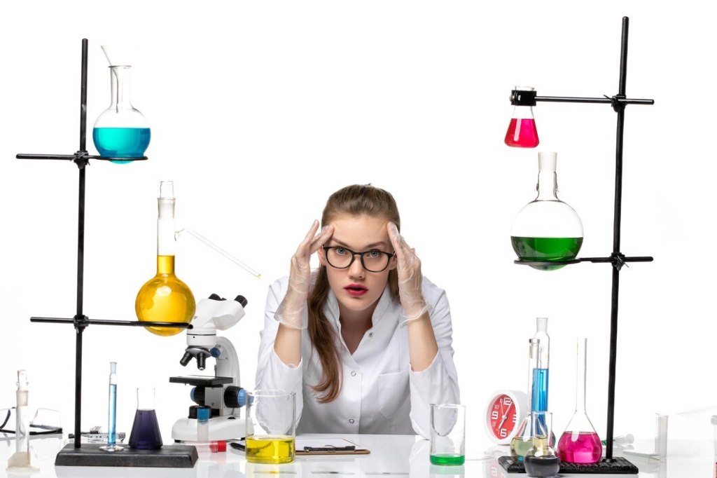 female chemist in medical suit in front of table with solutions