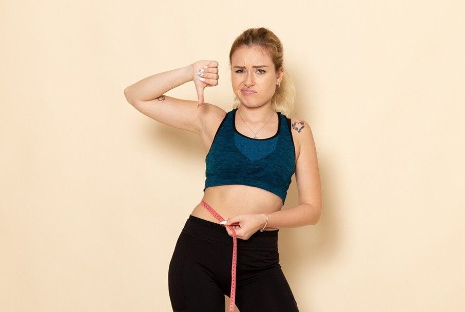 bulimia vs anorexia nervosa - young female in sport outfit measuring her body